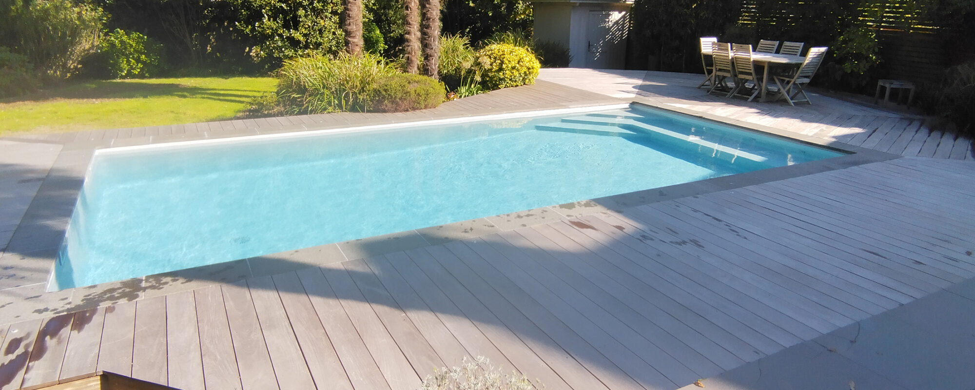 Piscine avec plage en bois et margelles en pierre